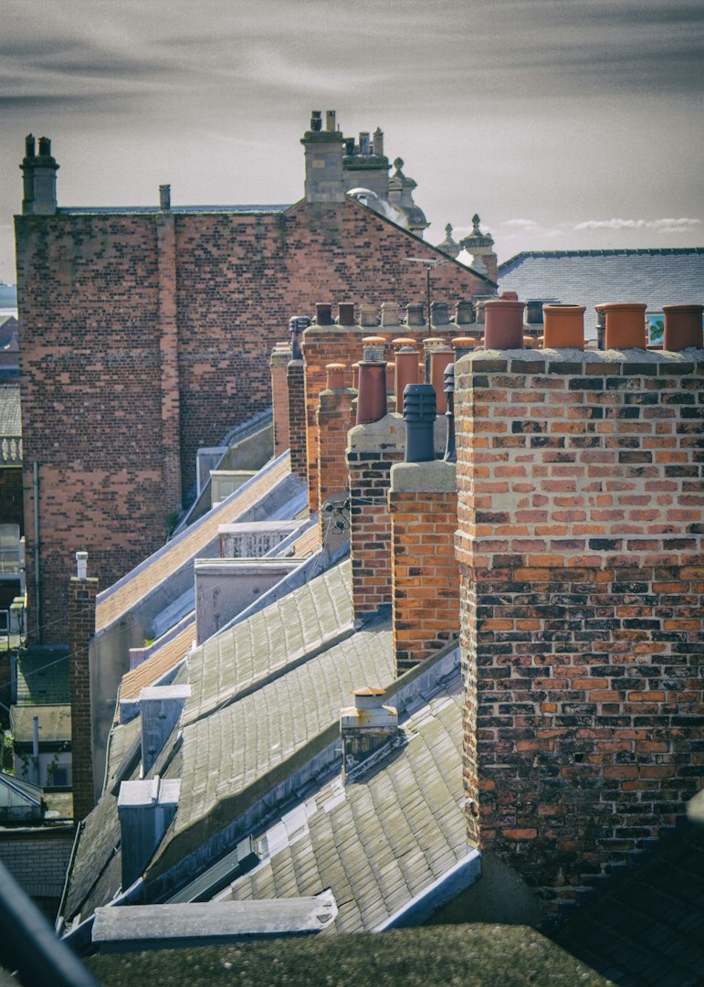UK terraced house pitched roofs repaired by a rooferwith red and black chimney pots and red bricks