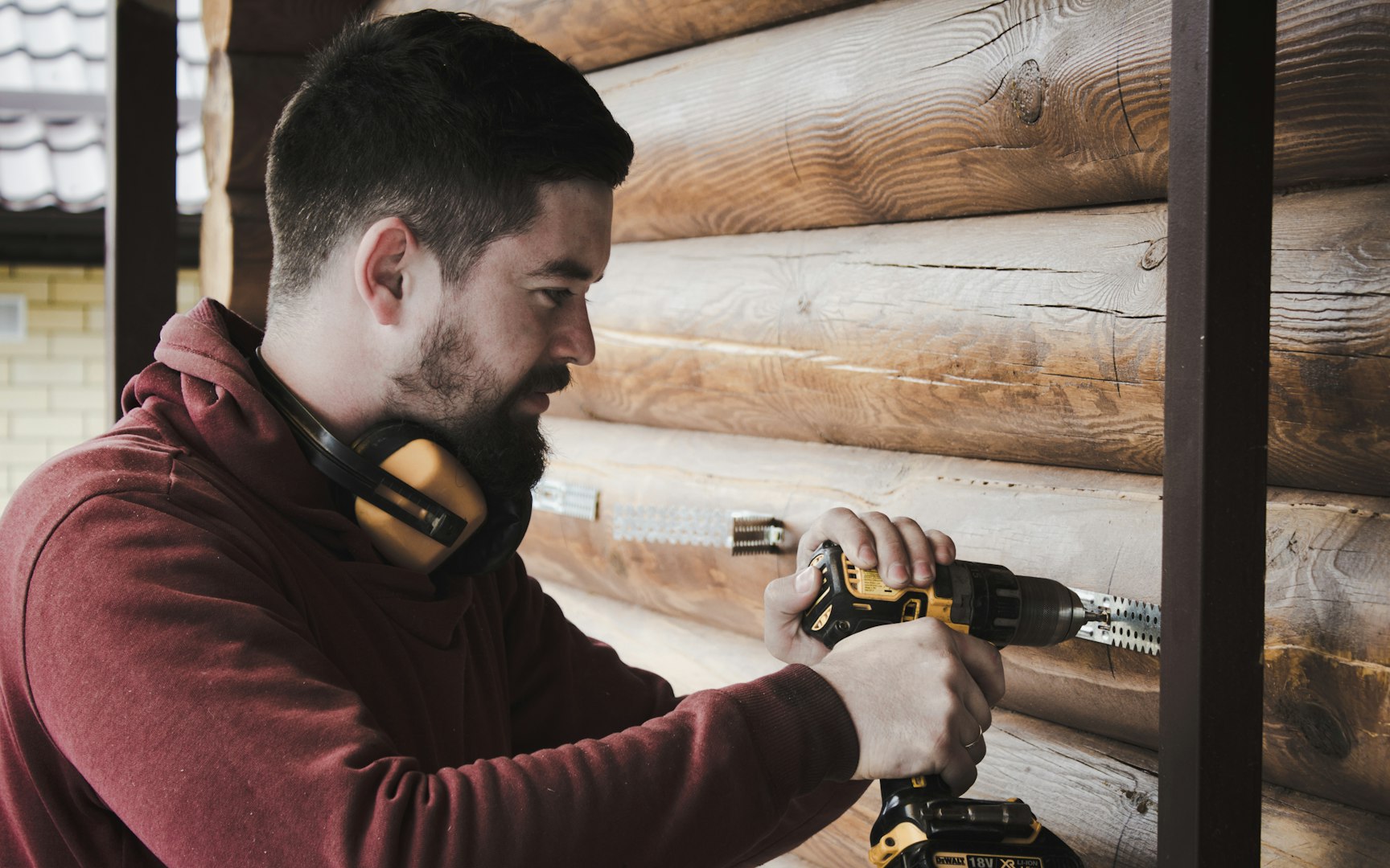 man with red jumper using black and yellow drill on wooden beams