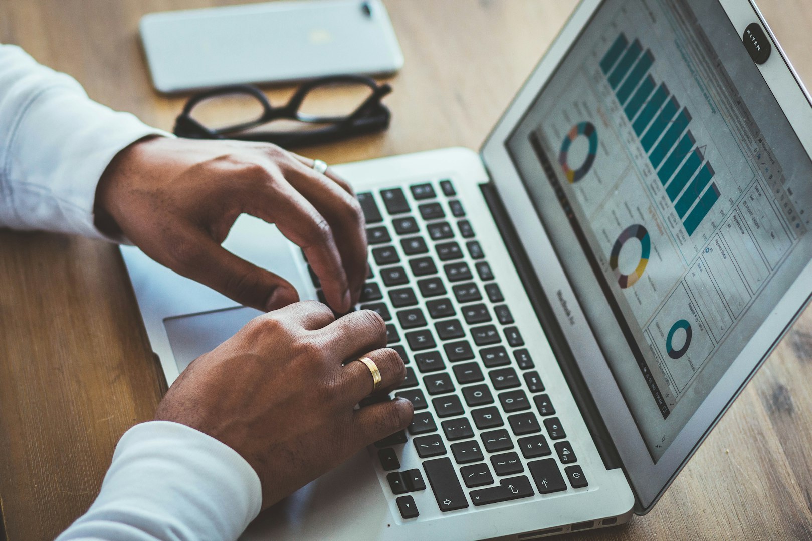 hands typing on a silver laptop on a brown table doing Google keyword research 
